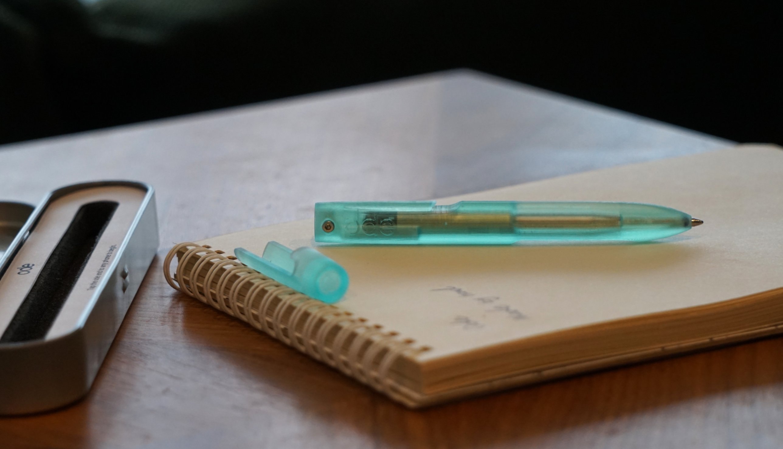 The Ode Pen and its cap resting on a notebook beside the open tin