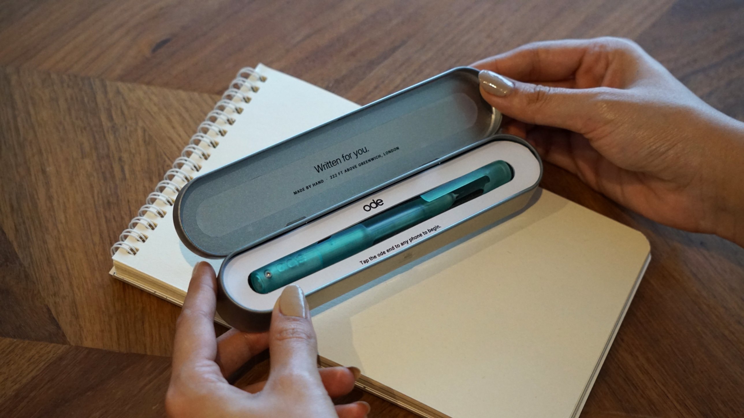 Hands opening the Ode tin: inside the lid it reads Written for you, and the pen rests in a white card