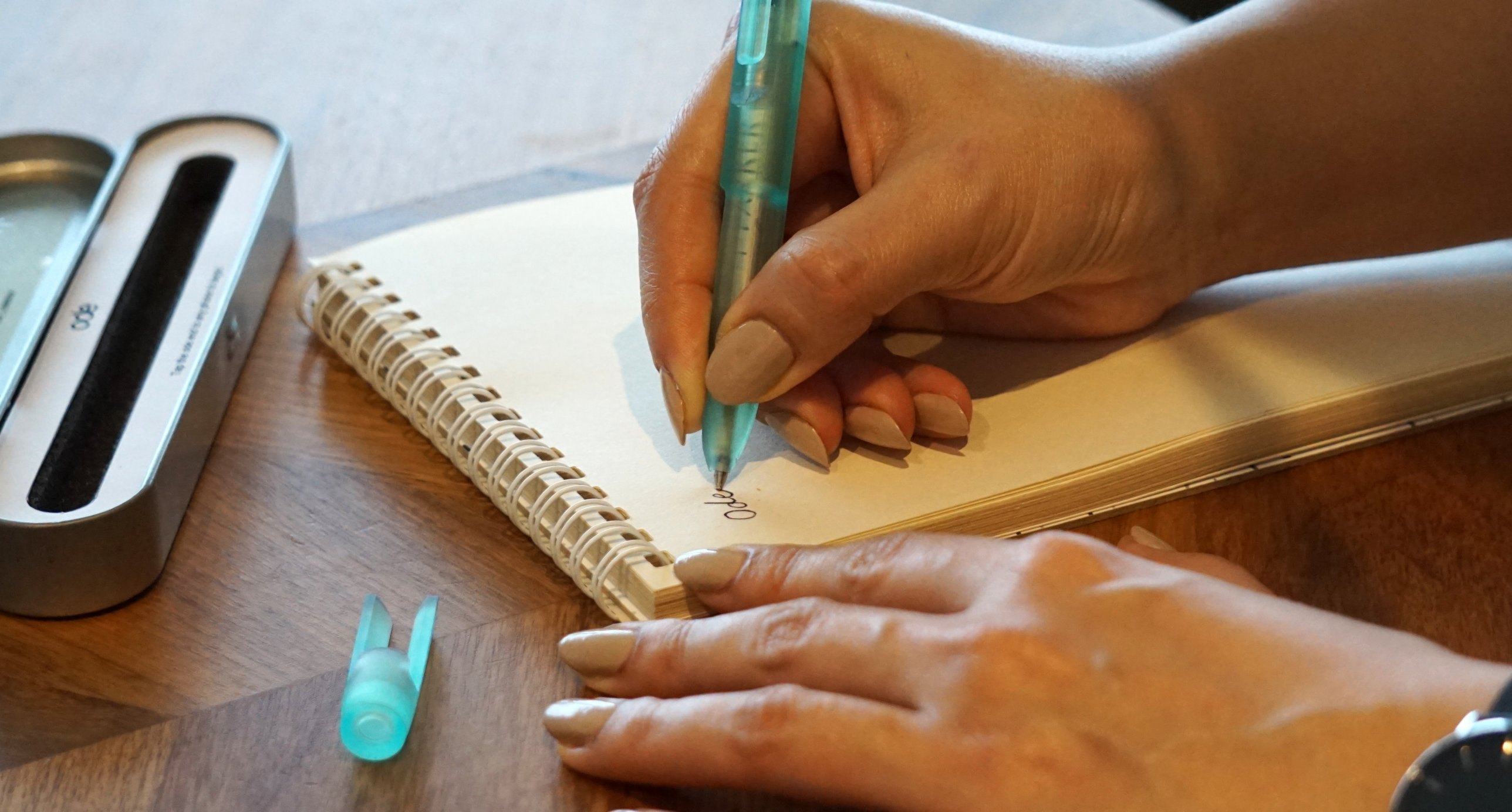 A hand writing the word Ode in a notebook with the emerald Ode Pen